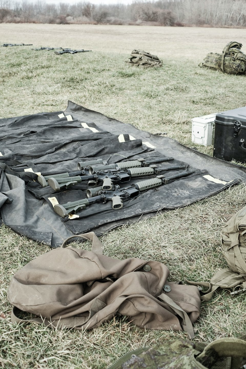 Rifles tácticos y equipo dispuestos sobre una alfombra en el campo.