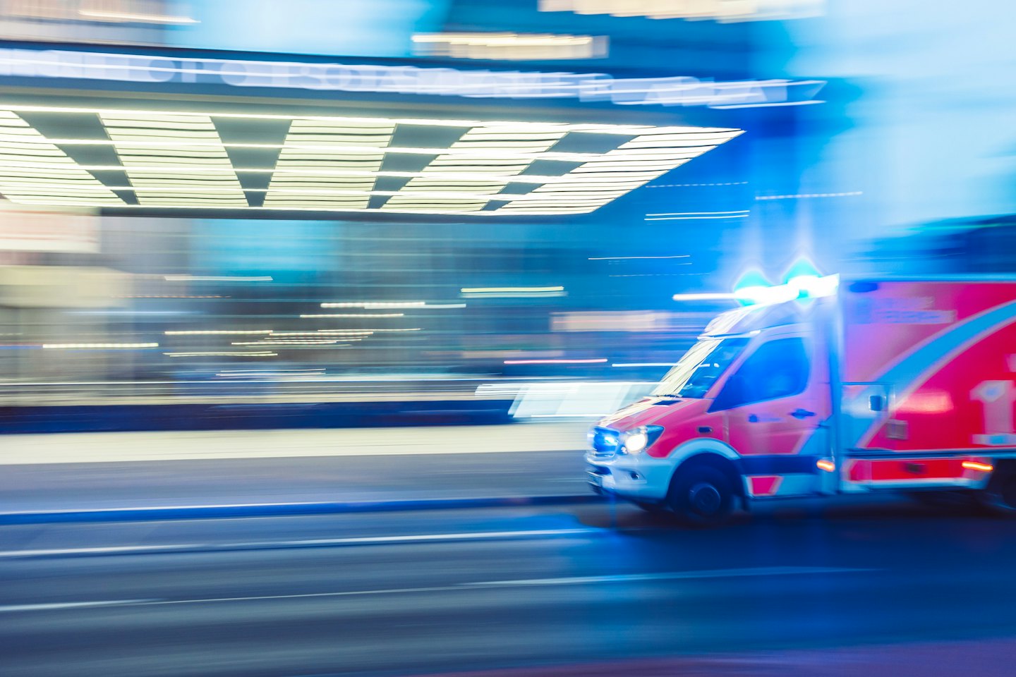 Ambulancia roja y blanca circulando a toda velocidad por una calle de la ciudad con luces azules intermitentes.
